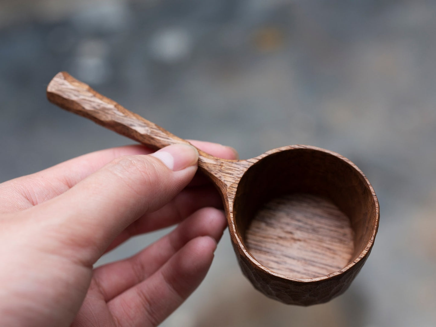 Close-up of a hand holding the faceted bowl of the walnut coffee scoop.