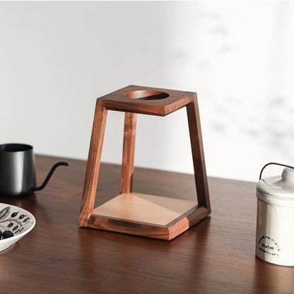 A minimalist, two-tone wood pour-over coffee stand on a dark wood desk.