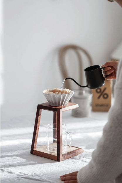 Pouring hot water into a ceramic dripper on the walnut coffee stand.