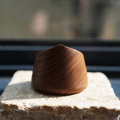 A small, carved walnut scent diffuser sitting on a stone in sunlight.