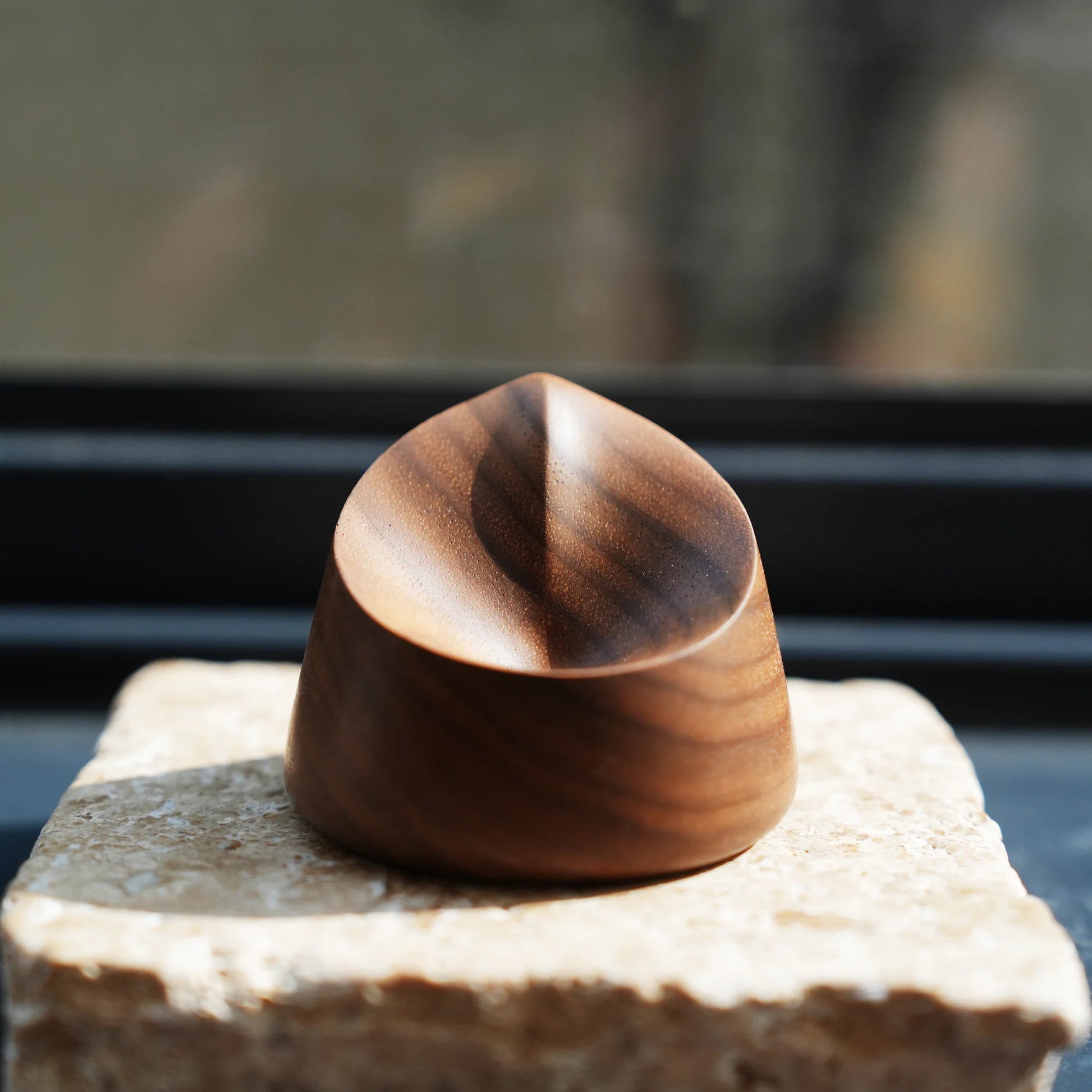 A small, carved walnut scent diffuser sitting on a stone in sunlight.