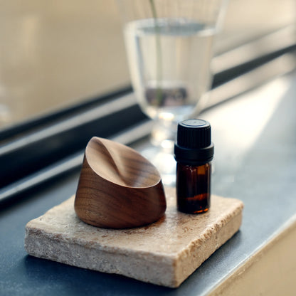 A minimalist walnut ring dish styled on a windowsill with an oil bottle.