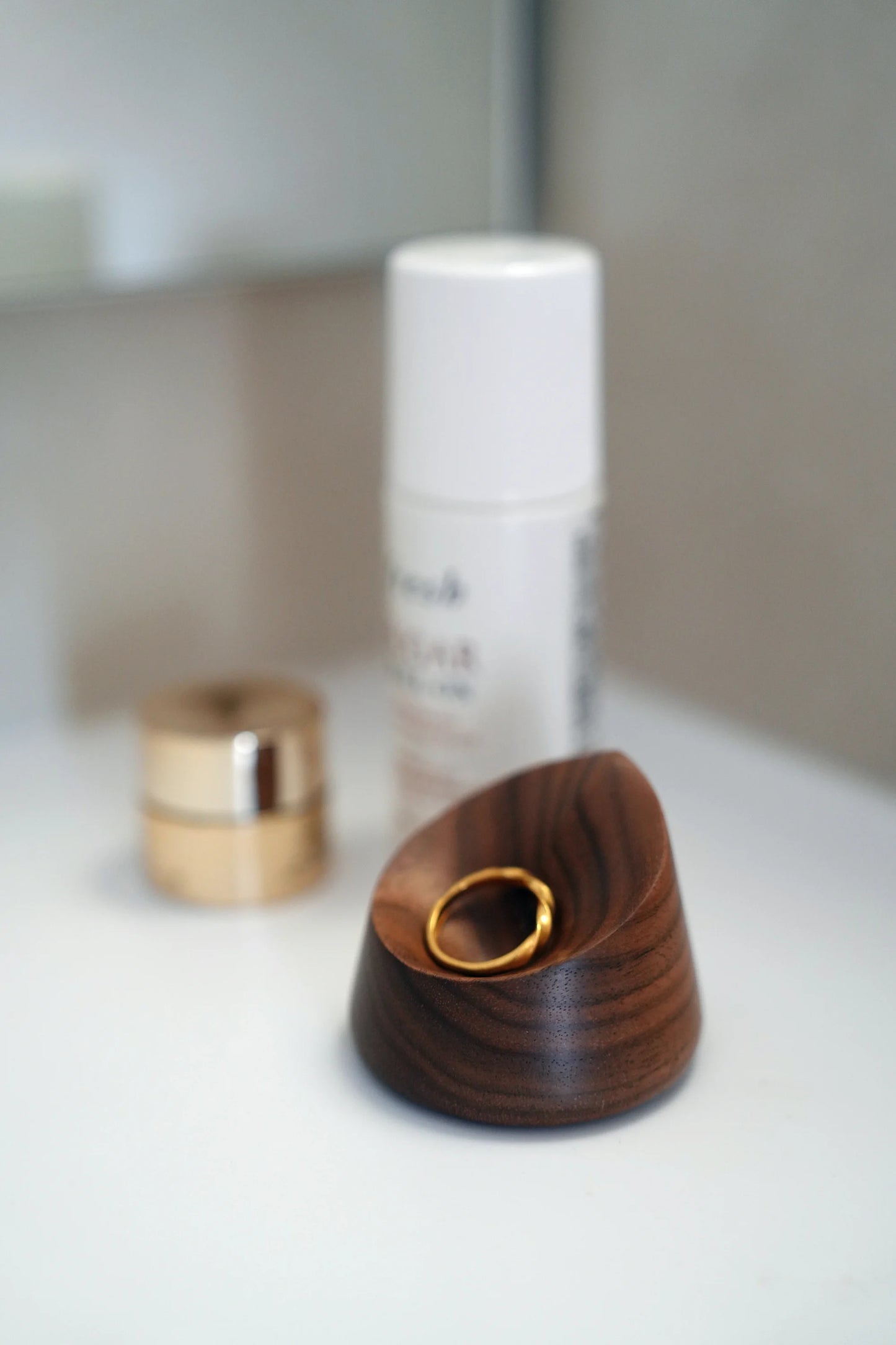 A gold ring resting in the smooth dish of a carved walnut holder.