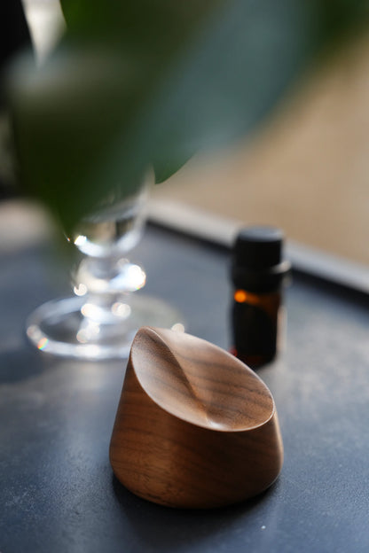 A carved walnut ring dish on a dark surface, seen through a green leaf.