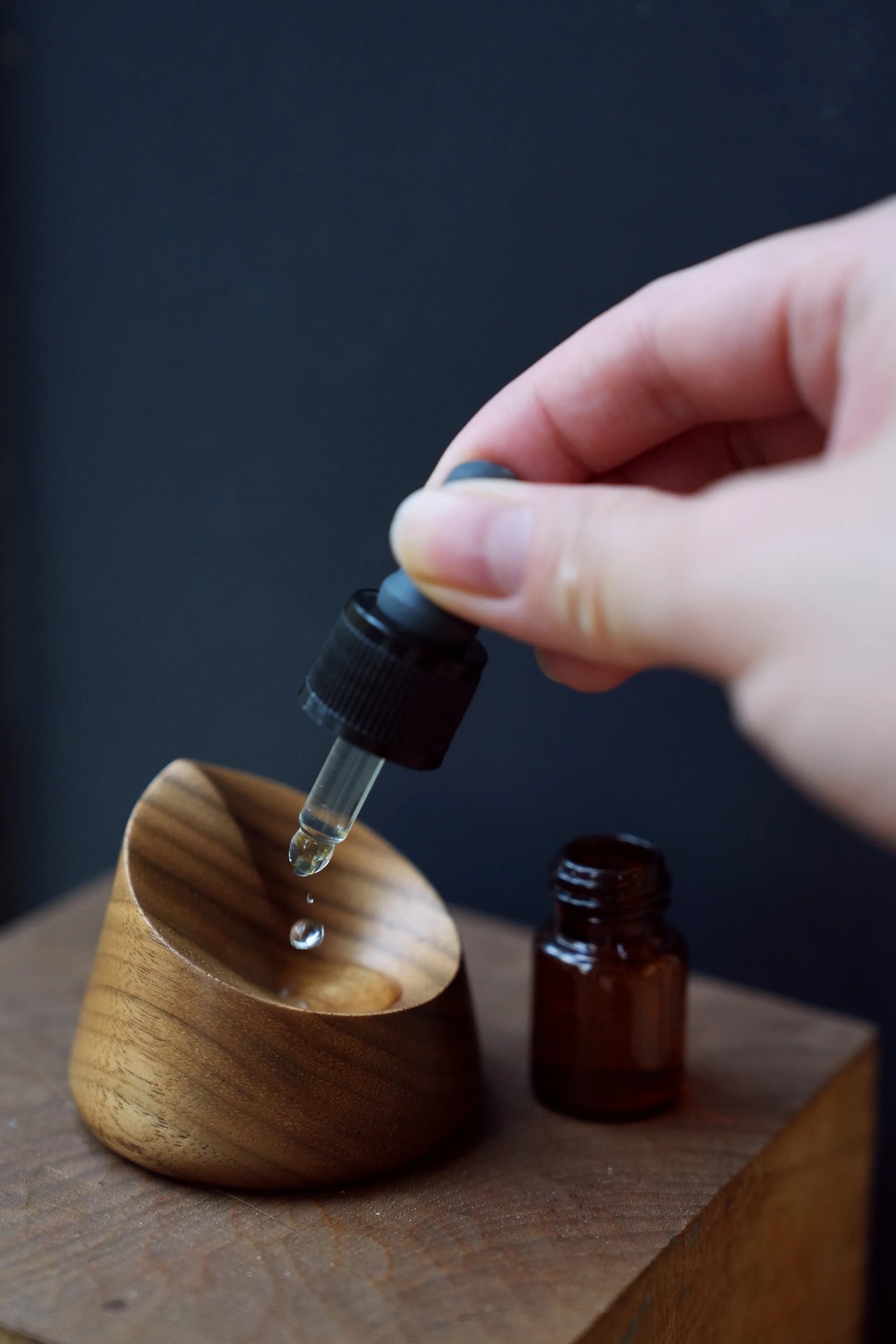 Hand dropping essential oil into a small, carved walnut diffuser dish.
