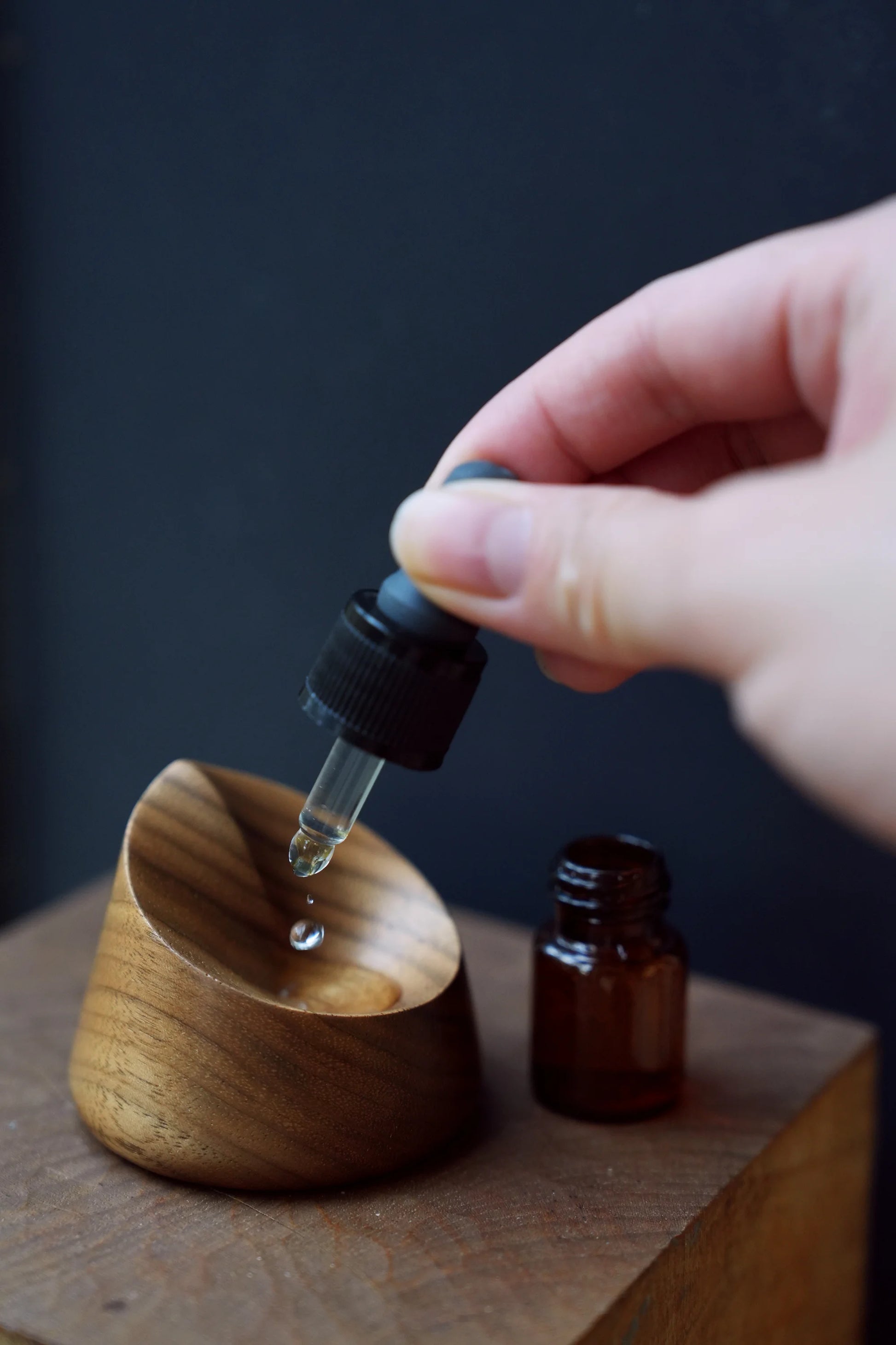 Hand dropping essential oil into a small, carved walnut diffuser dish.