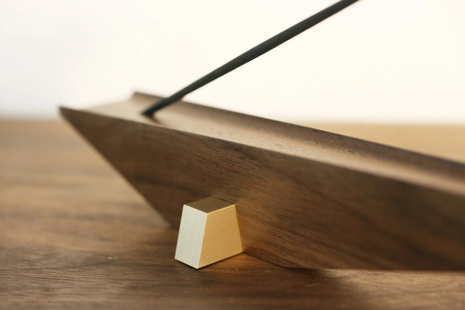 Close-up of an architectural incense holder showing the brass foot and walnut grain.