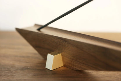 Close-up of an architectural incense holder showing the brass foot and walnut grain.