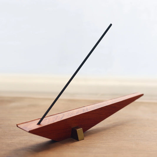 A minimalist architectural incense holder burning a stick of incense on a table.