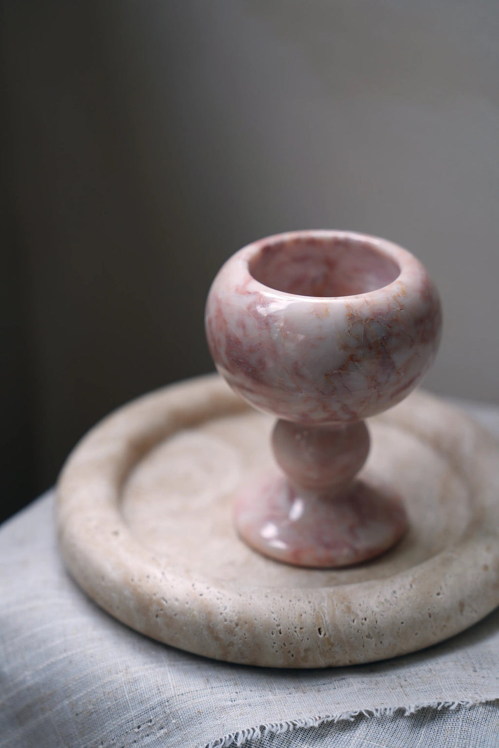 A hand-carved, pink marble ritual goblet on a travertine tray.