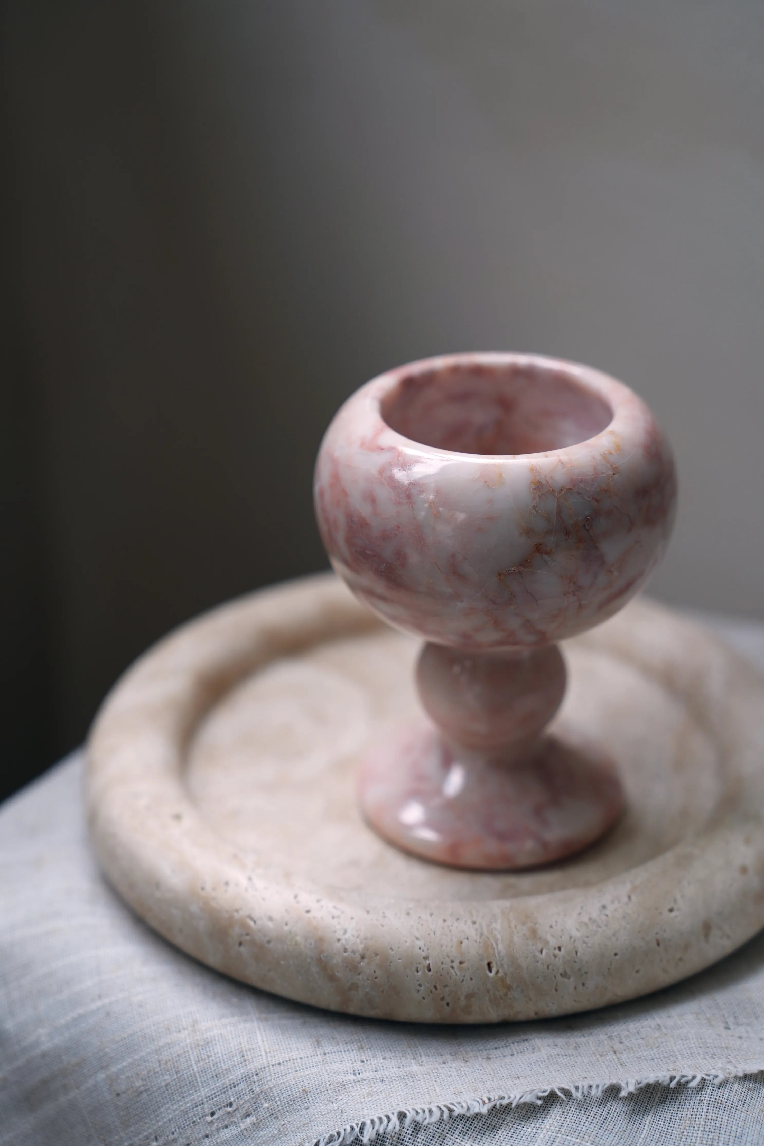 A hand-carved, pink marble ritual goblet on a travertine tray.