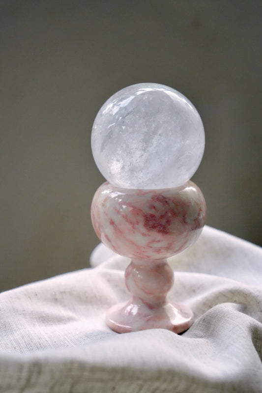A large, clear quartz crystal sphere resting in a pink marble goblet.
