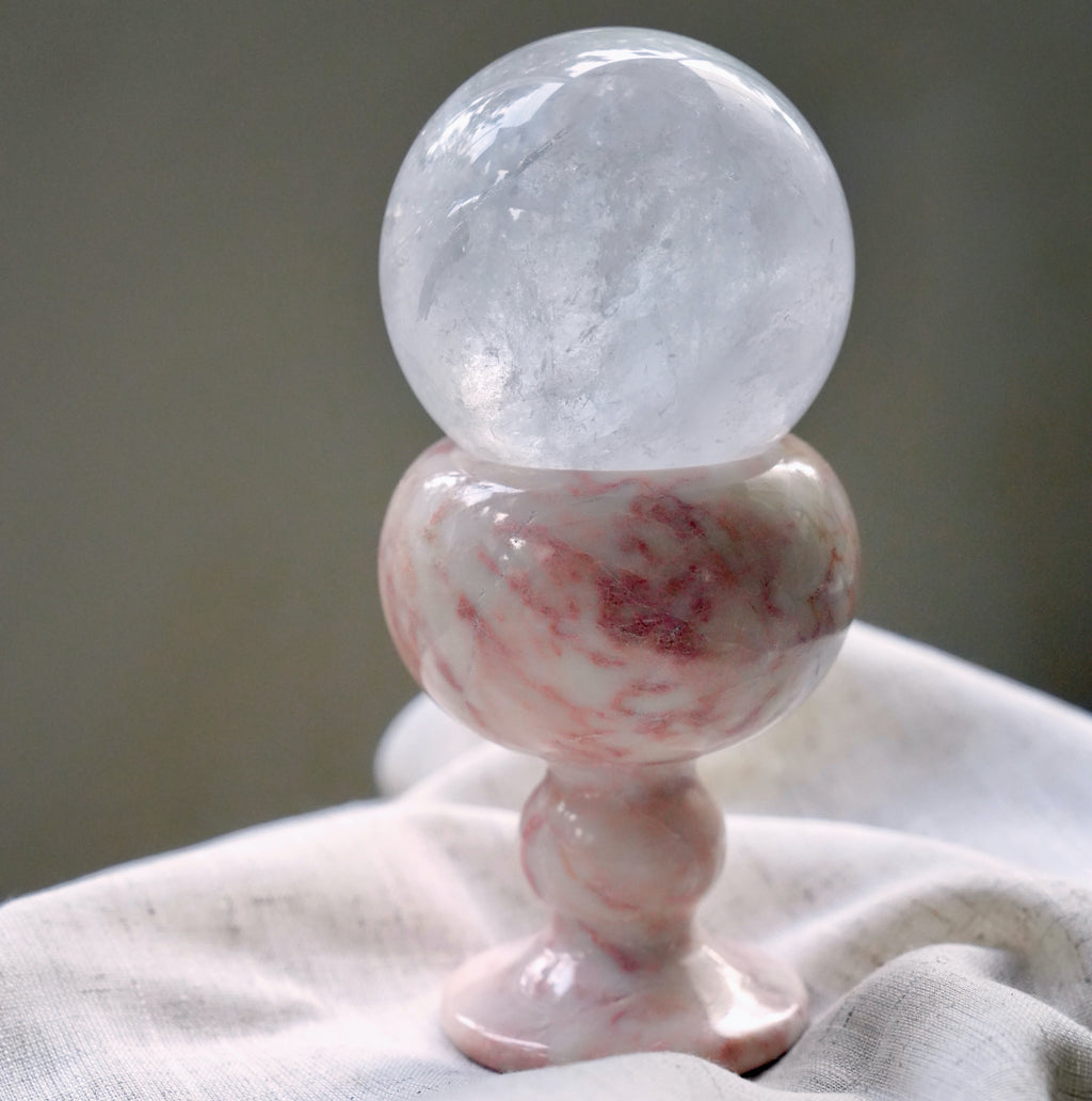 A large, clear quartz crystal sphere resting in a pink marble goblet.