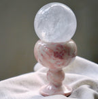 A large, clear quartz crystal sphere resting in a pink marble goblet.