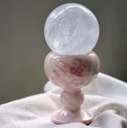 A large, clear quartz crystal sphere resting in a pink marble goblet.