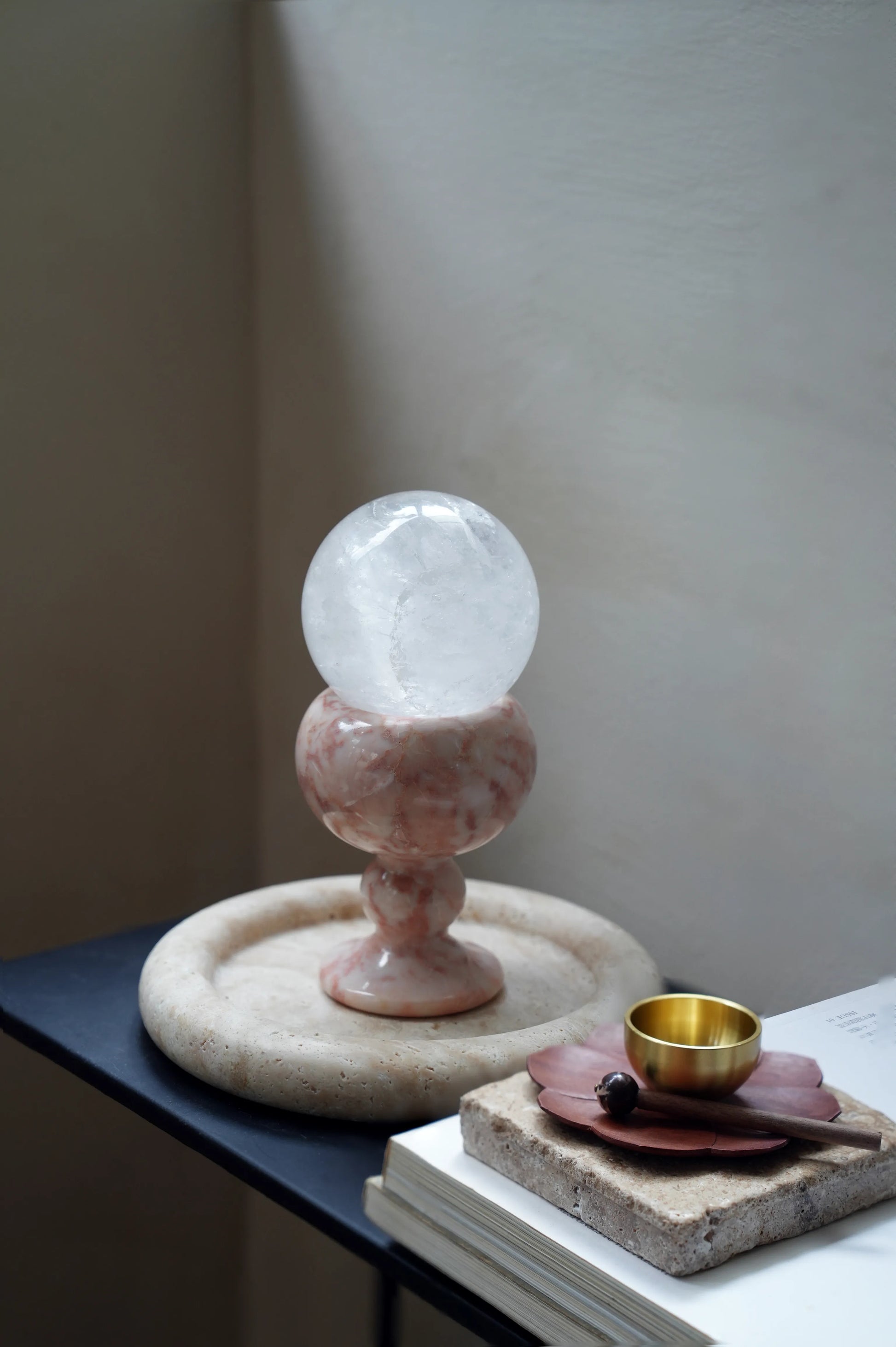 A pink marble crystal holder and a brass singing bowl on a modern table.