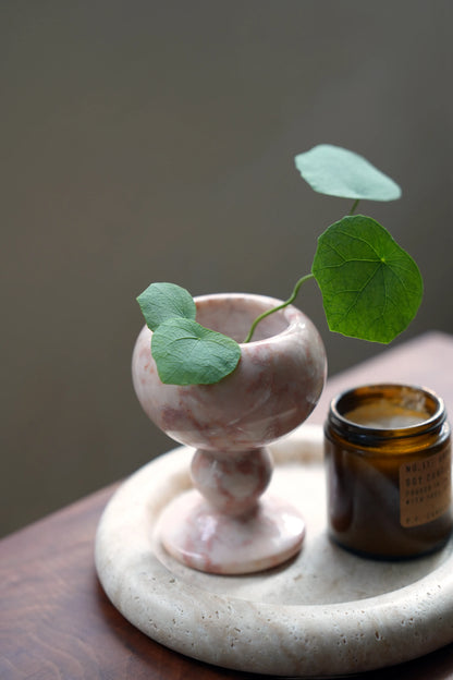A small green plant stem arranged in a pink marble bud vase.