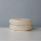 Two handmade alabaster bowls stacked, showing the Solid Cloud style on top and the Veined Stratus style below, against a pale blue-grey background.