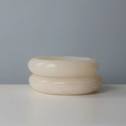 Two handmade alabaster bowls stacked, showing the Solid Cloud style on top and the Veined Stratus style below, against a pale blue-grey background.