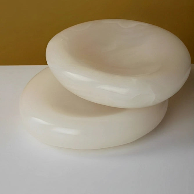 An angled view of two polished alabaster bowls stacked, highlighting their smooth, glossy finish and organic shape against a warm gold background.