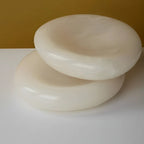 An angled view of two polished alabaster bowls stacked, highlighting their smooth, glossy finish and organic shape against a warm gold background.