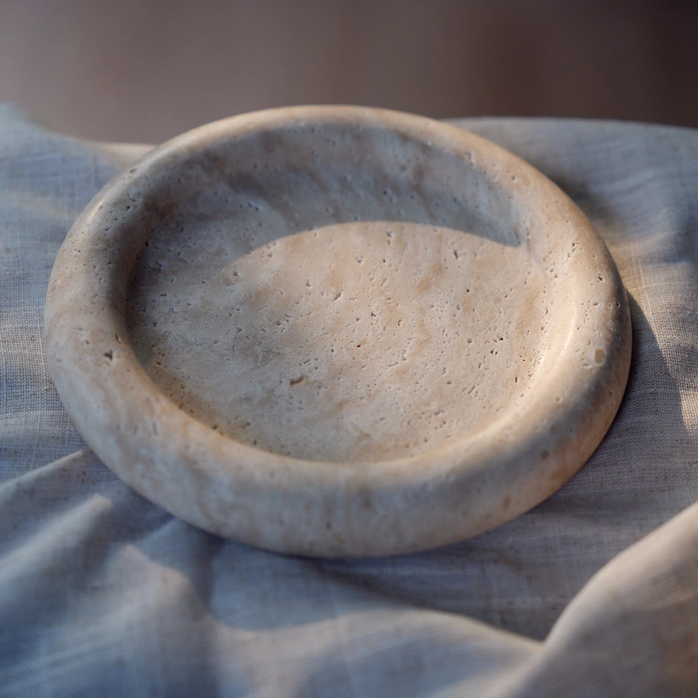 The empty travertine tray sitting on a soft, neutral-colored linen cloth, with gentle light emphasizing its porous texture.