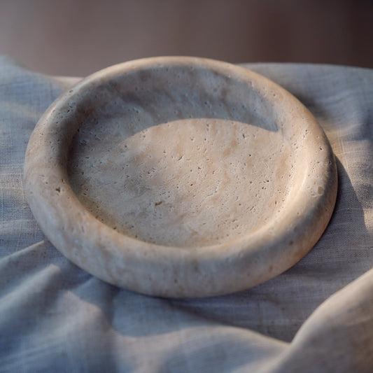 The empty travertine tray sitting on a soft, neutral-colored linen cloth, with gentle light emphasizing its porous texture.