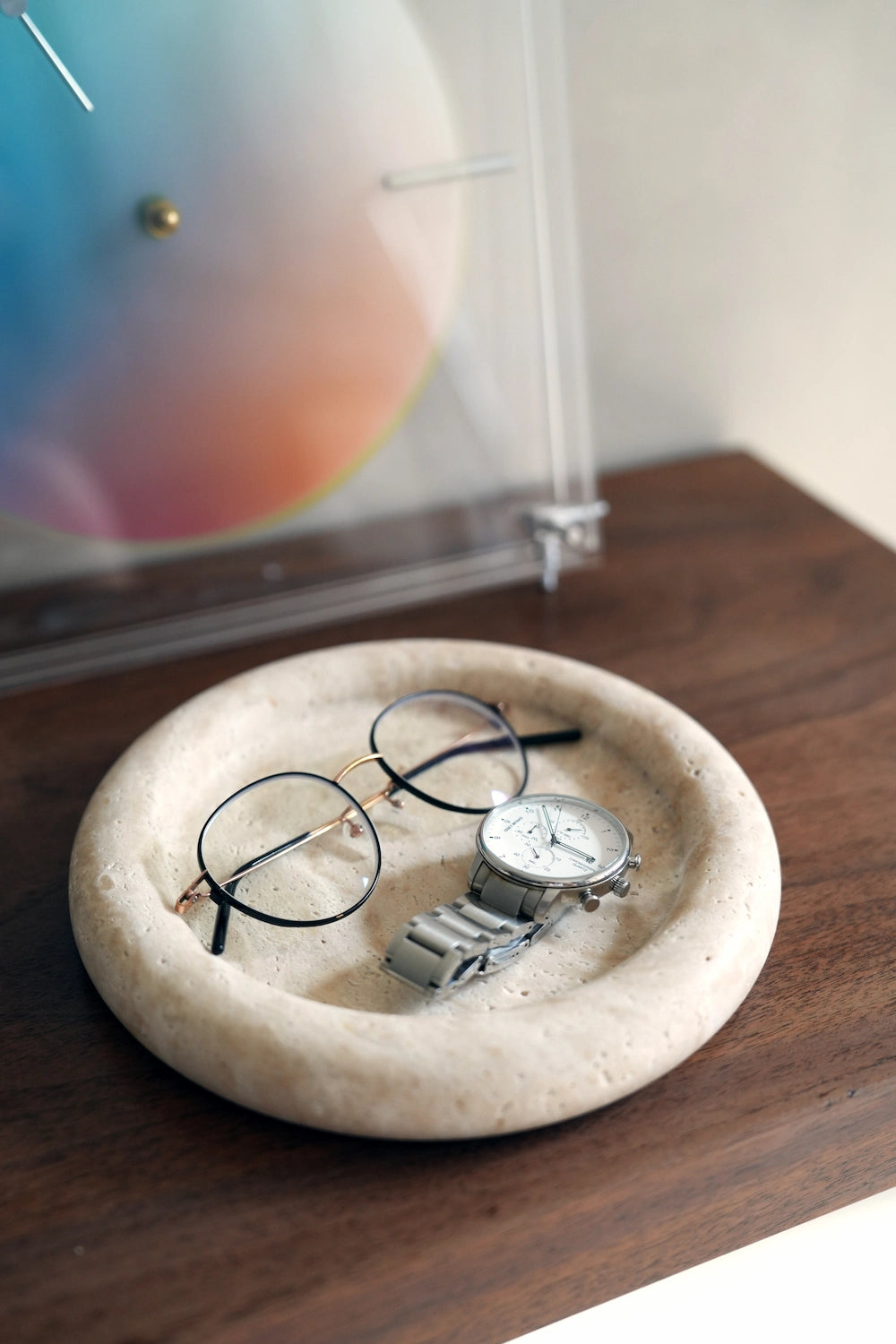 Eyeglasses and a watch placed within the round travertine tray, demonstrating its function as a stylish catchall on a desk.