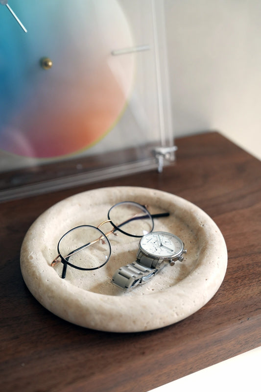 Eyeglasses and a watch placed within the round travertine tray, demonstrating its function as a stylish catchall on a desk.