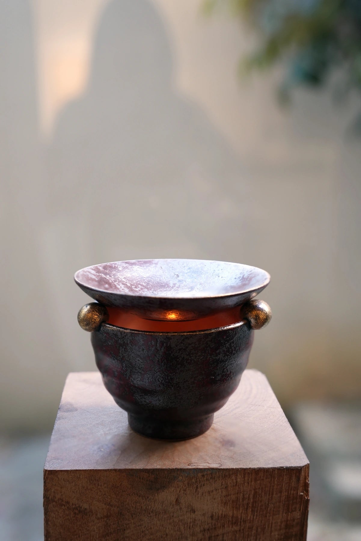 Handcrafted ceramic oil burner, front view, on wood pedestal
