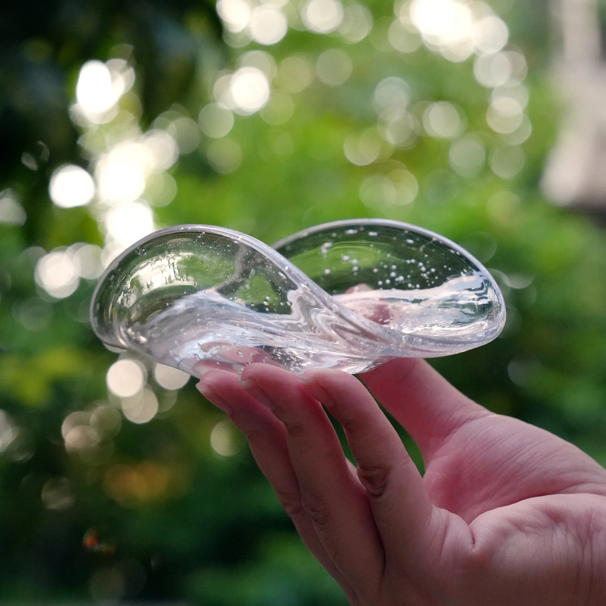 Hand holding a clear, bubble glass incense dish against a green background.