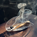 Smoke rising from a Palo Santo stick in a bubble glass dish in sunlight.