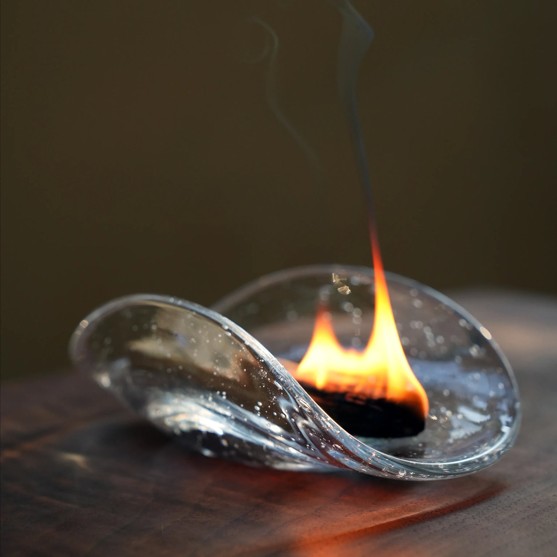 A Palo Santo stick burning with a flame inside a clear glass dish.