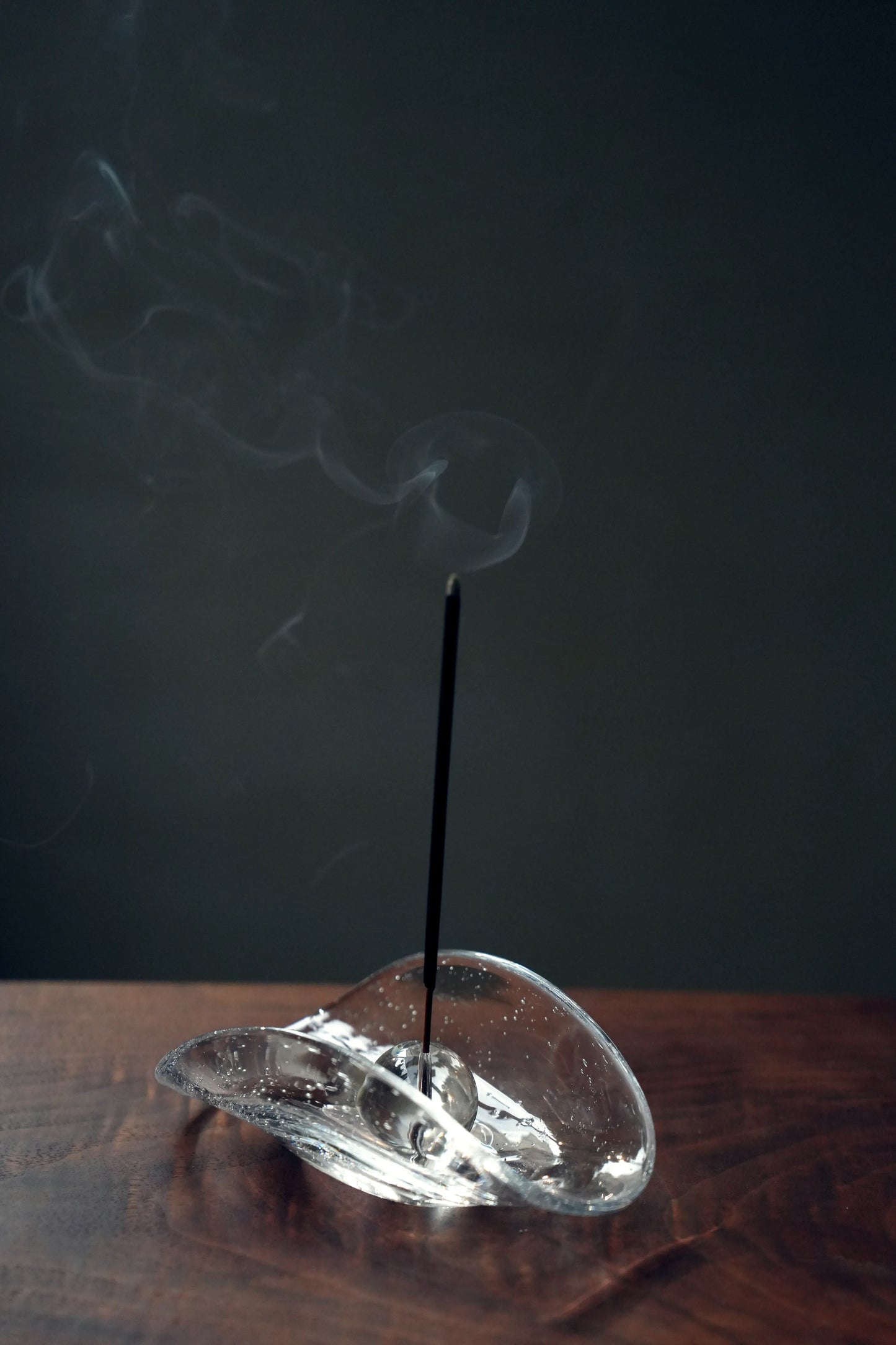 An incense stick burning in the sphere holder of a bubble glass dish.