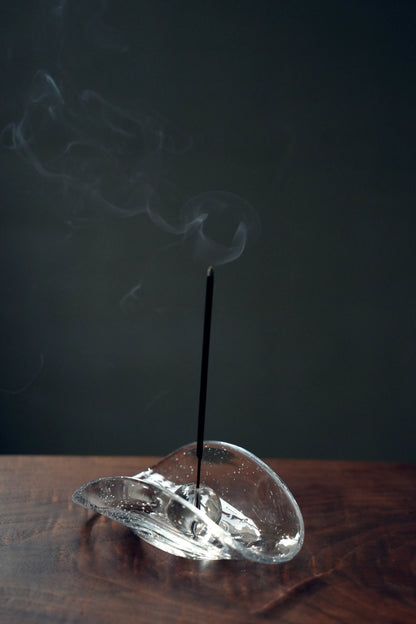 An incense stick burning in the sphere holder of a bubble glass dish.