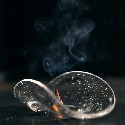 An incense cone smoldering in a bubble glass dish on a black surface.