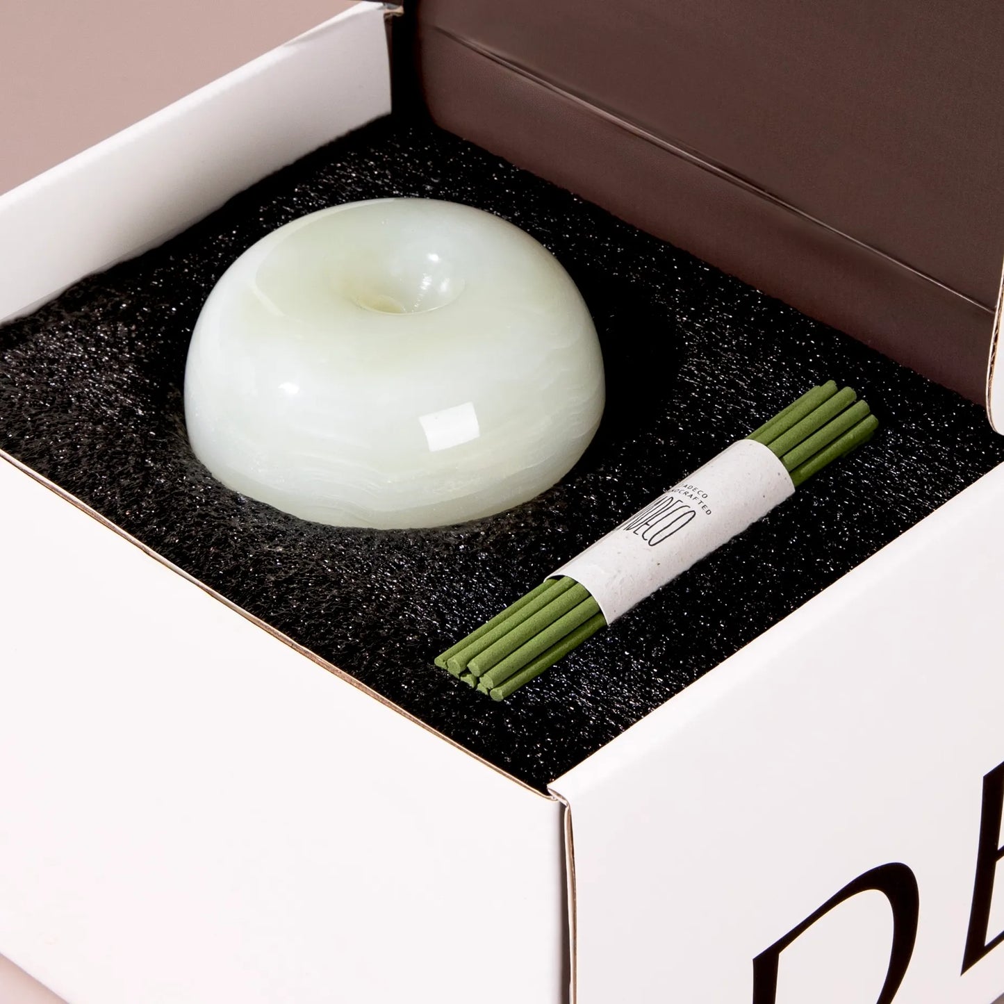 An apple-shaped onyx incense holder with a bundle of green incense.