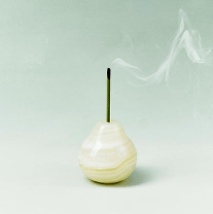 A pale, translucent onyx pear incense holder with smoke against a green wall.