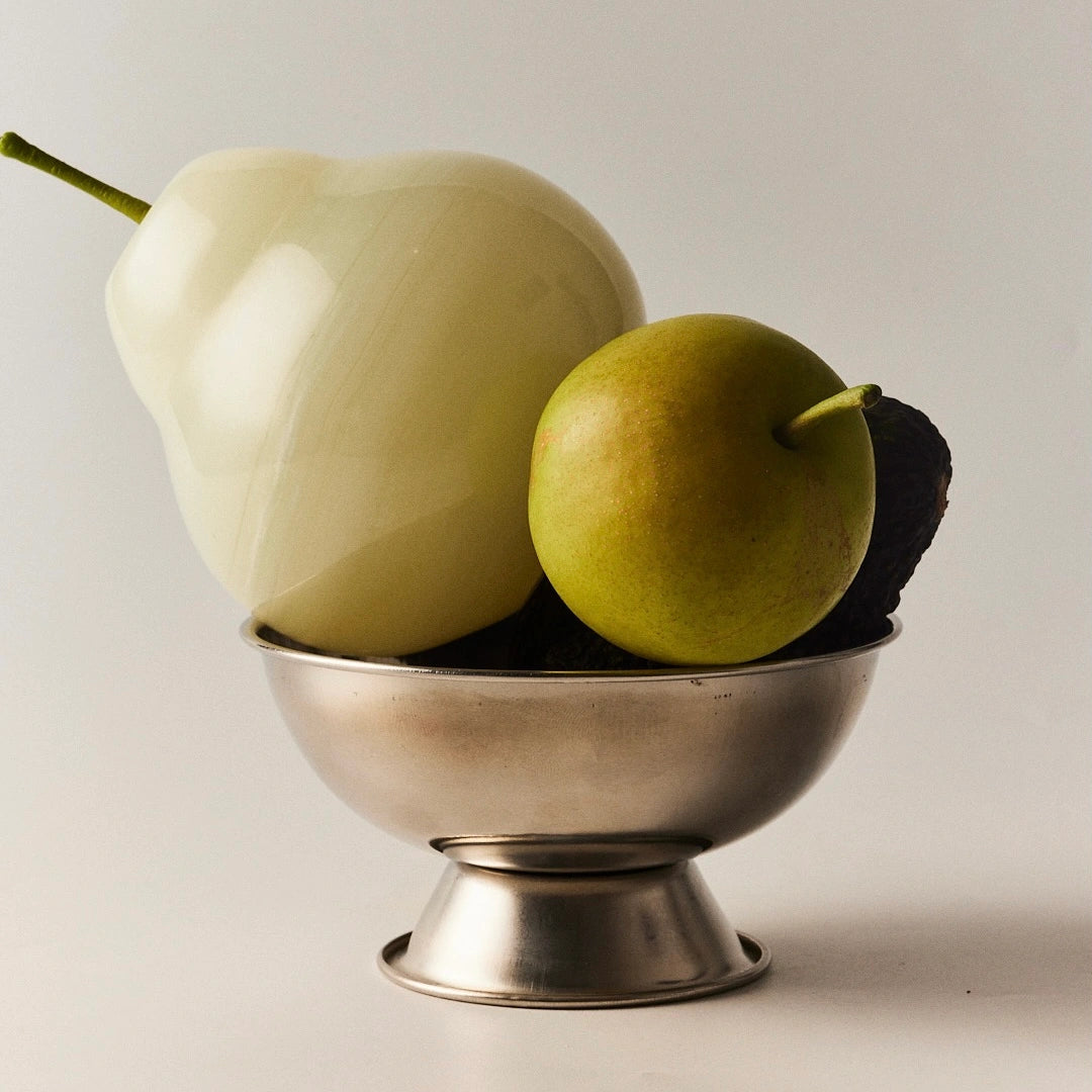 A still life of a white onyx pear next to a real green pear in a bowl.