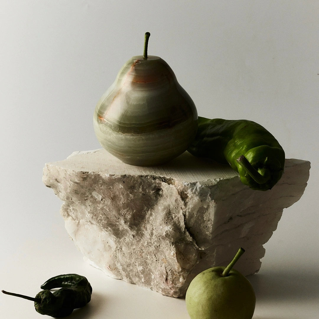 A green onyx pear sculpture styled on a block of raw stone.