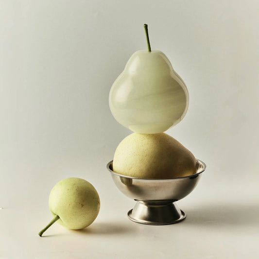 A translucent onyx pear balancing on top of a real pear in a bowl.