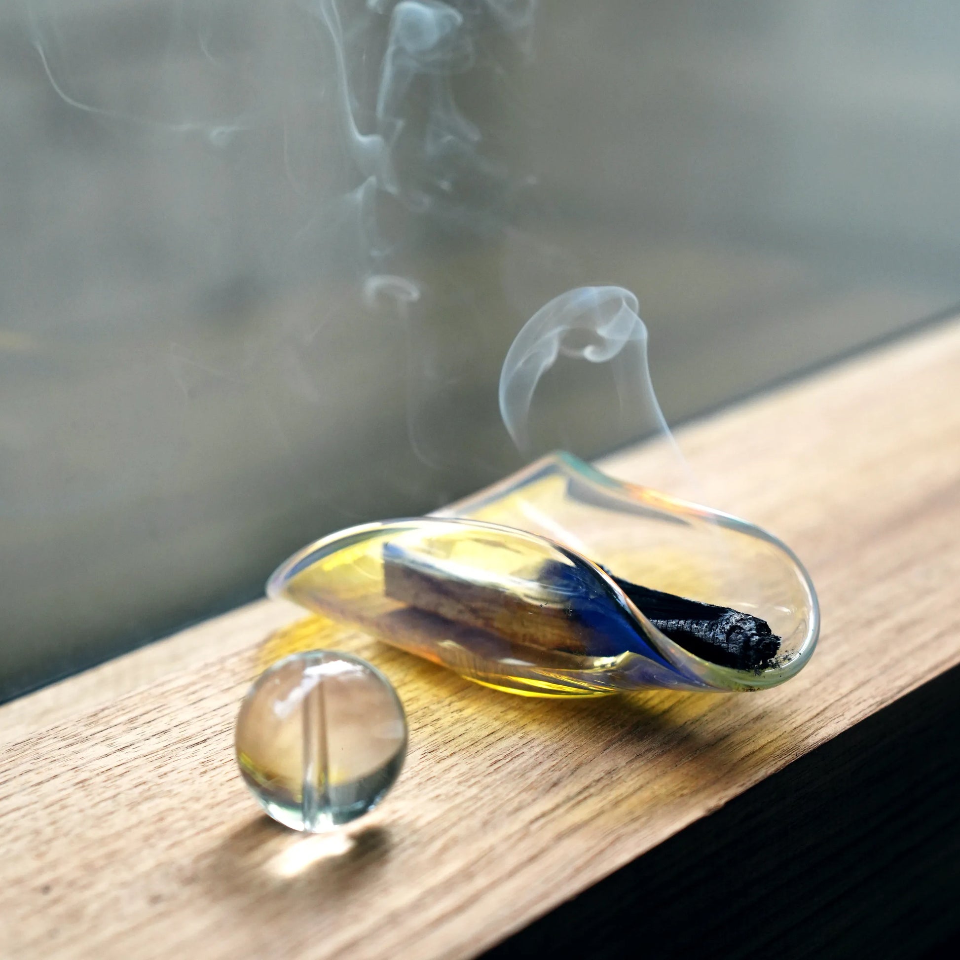 A smoldering Palo Santo stick resting in an iridescent glass holder.