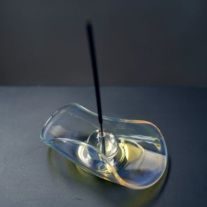 An incense stick burning in the sphere of an iridescent glass holder.