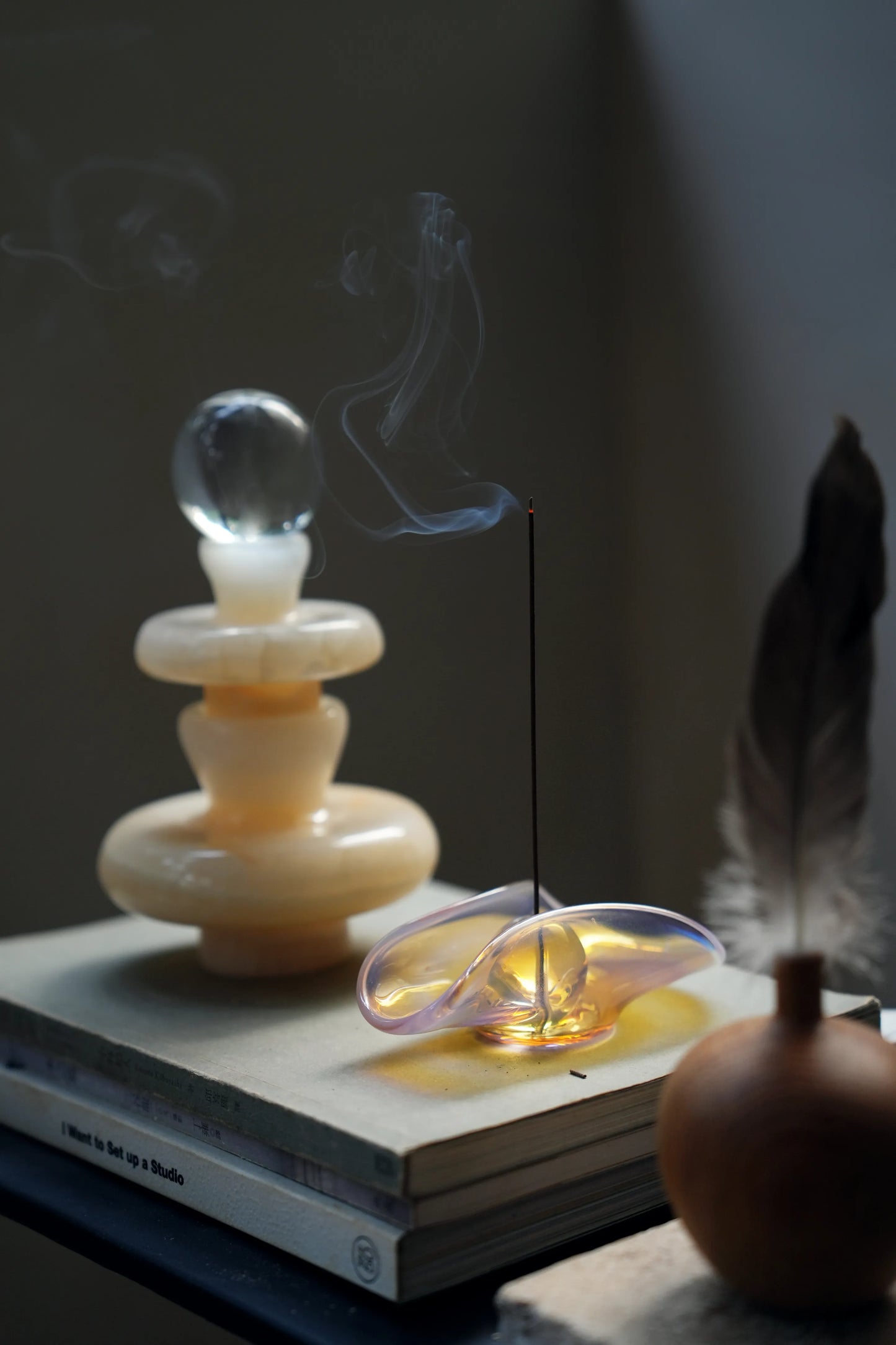 A pink iridescent incense holder styled on a book next to a sculpture.