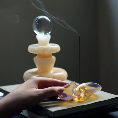 Hand adjusting an iridescent glass incense dish with smoke rising.