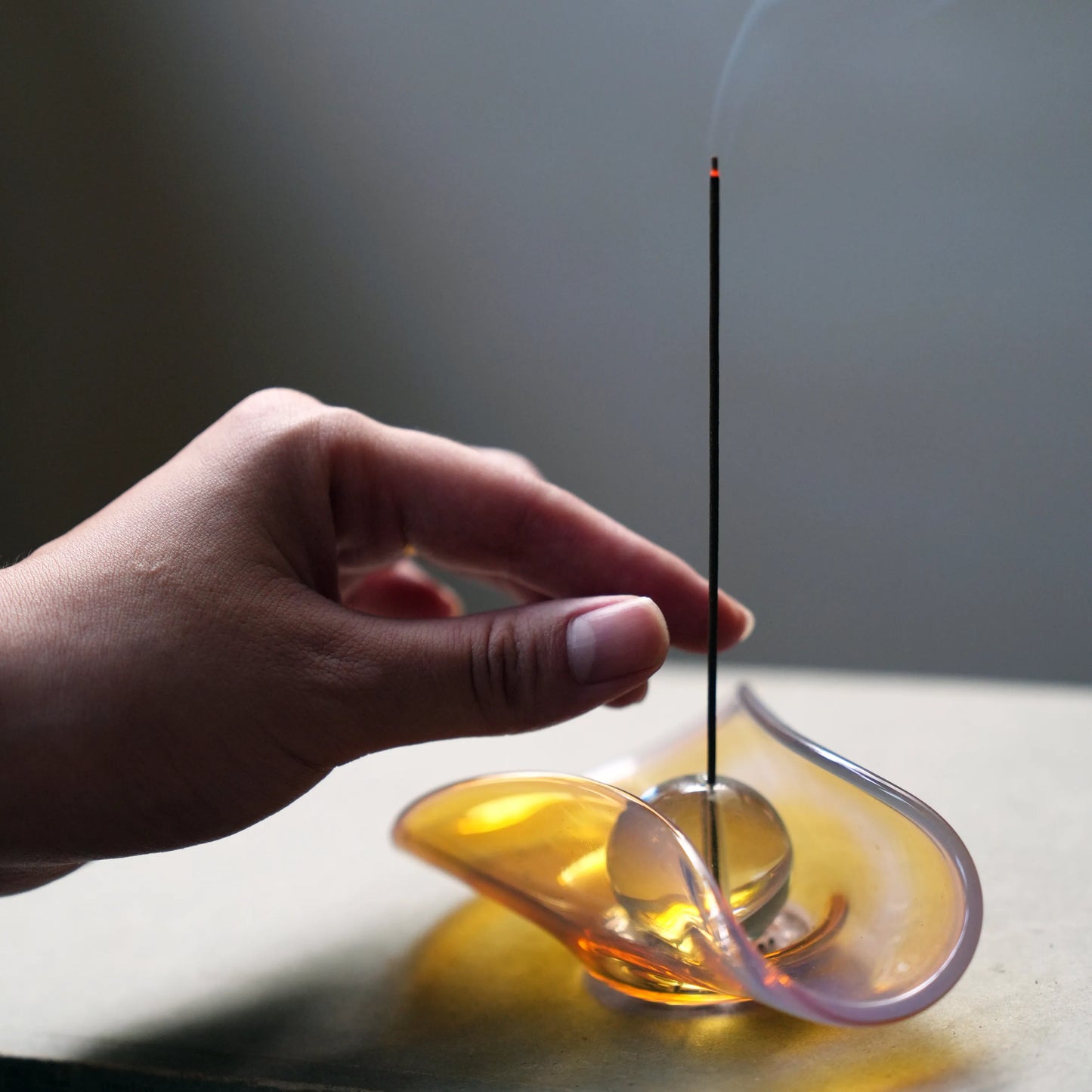 Hand reaching for an incense stick in a glowing glass holder.
