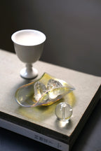 An iridescent glass dish holding two small quartz crystals on a book.