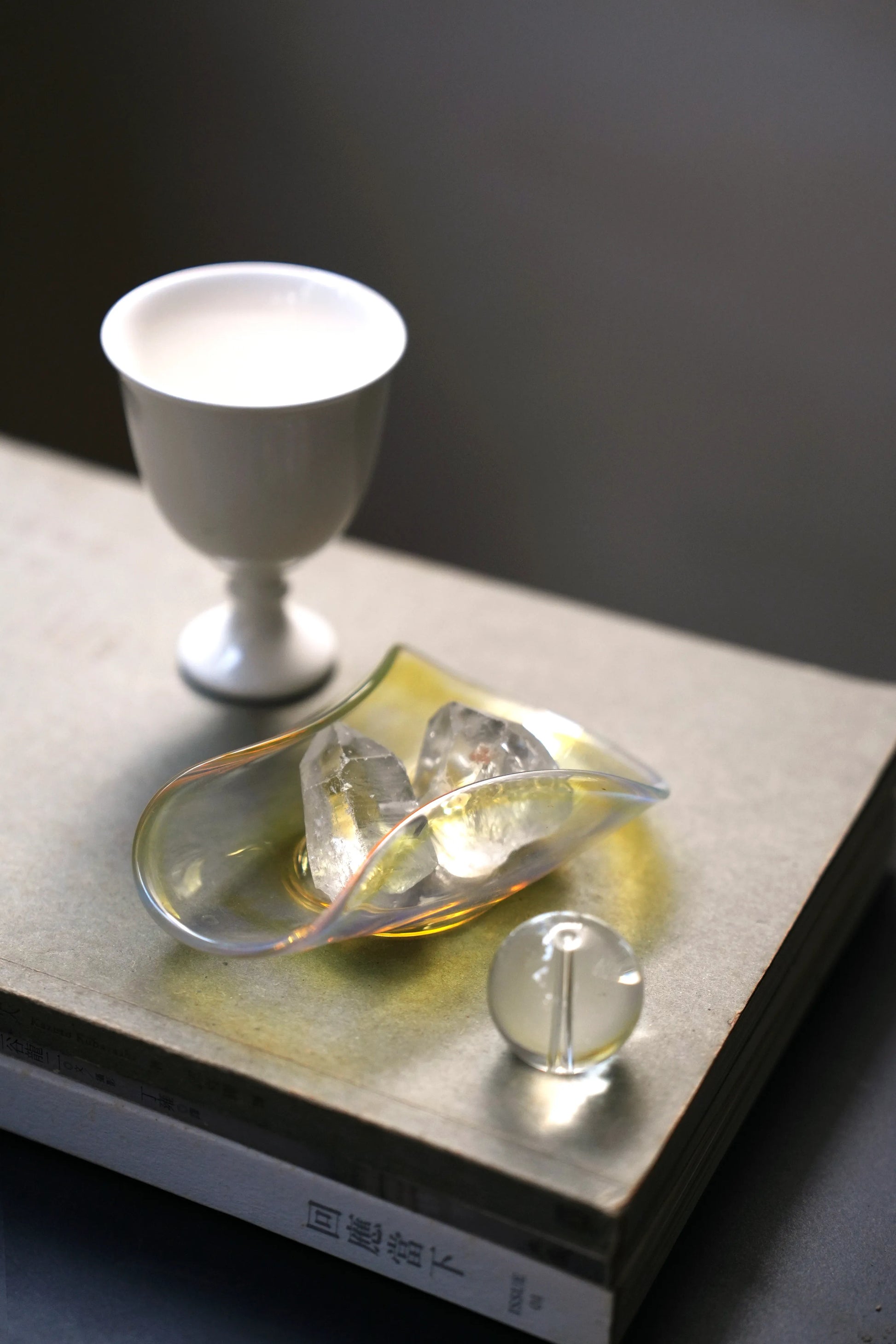 An iridescent glass dish holding two small quartz crystals on a book.