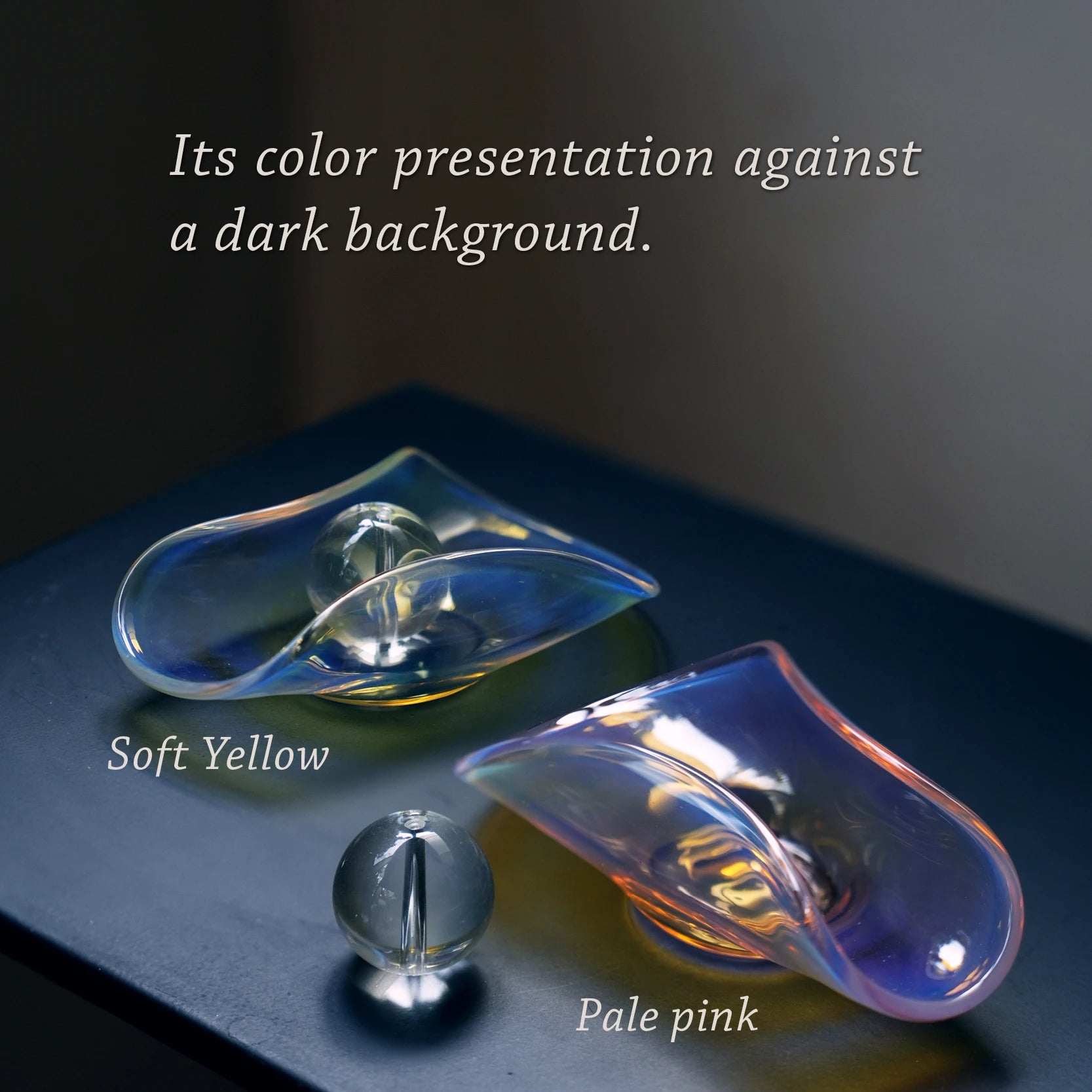 Two iridescent glass incense holders in yellow and pink on a dark surface.