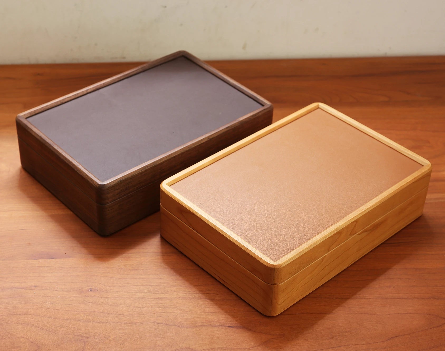 Two wood jewelry boxes, one cherry and one walnut, on a wood table.